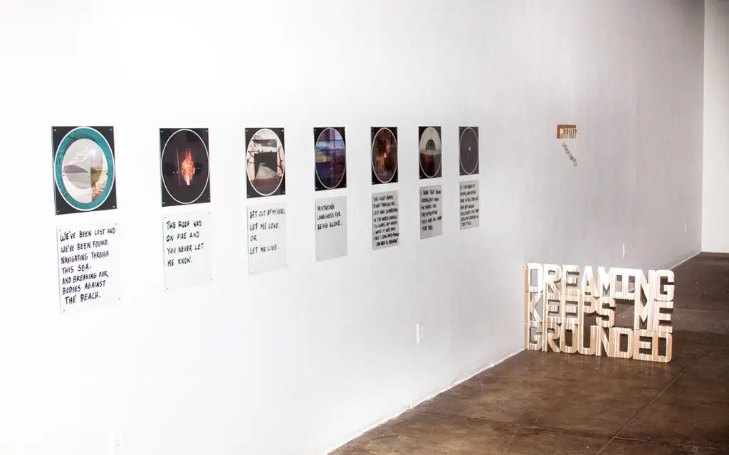 Installation art of 3D typography with the phrase dreaming keeps me grounded and photography pieces on a gallery wall.